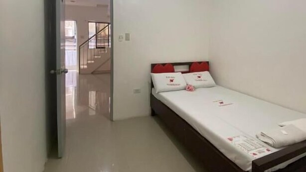 A small, clean room with a single bed, a door leading to a staircase, and an air conditioning unit on the wall.