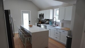 Une cuisine moderne avec des meubles blancs, un îlot central doté de tabourets, un réfrigérateur en acier inoxydable et un four à micro-ondes placé au-dessus de la cuisinière.