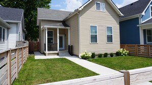 Une maison à deux étages avec un porche à l’avant, un petit jardin et une clôture en bois.