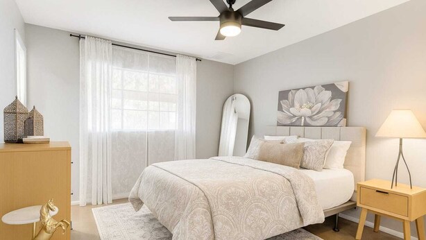 A bedroom with a bed, bedside table, lamp, decorative items, and a window with curtains.