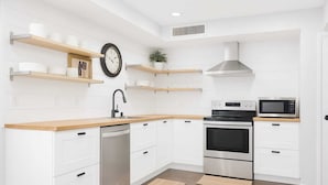 A modern kitchen with white cabinets, stainless steel appliances, wooden countertops, and a clock on the wall.