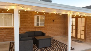 An outdoor patio with a brick wall, a covered seating area with a table, and string lights.
