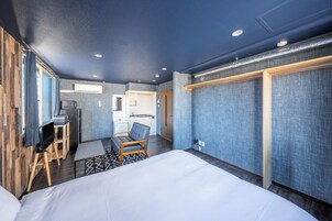 A hotel room with a bed, a desk with a chair, a kitchenette, and a sliding door closet.