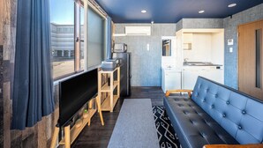 Ein modernes Interieur mit einer Couch, einem Fernseher, einer Küchenzeile und einem großen Fenster.