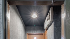 Ein schmaler Flur mit einer Holztür am Ende, einer Lampe darüber und einem kleinen Schrank zur Rechten.