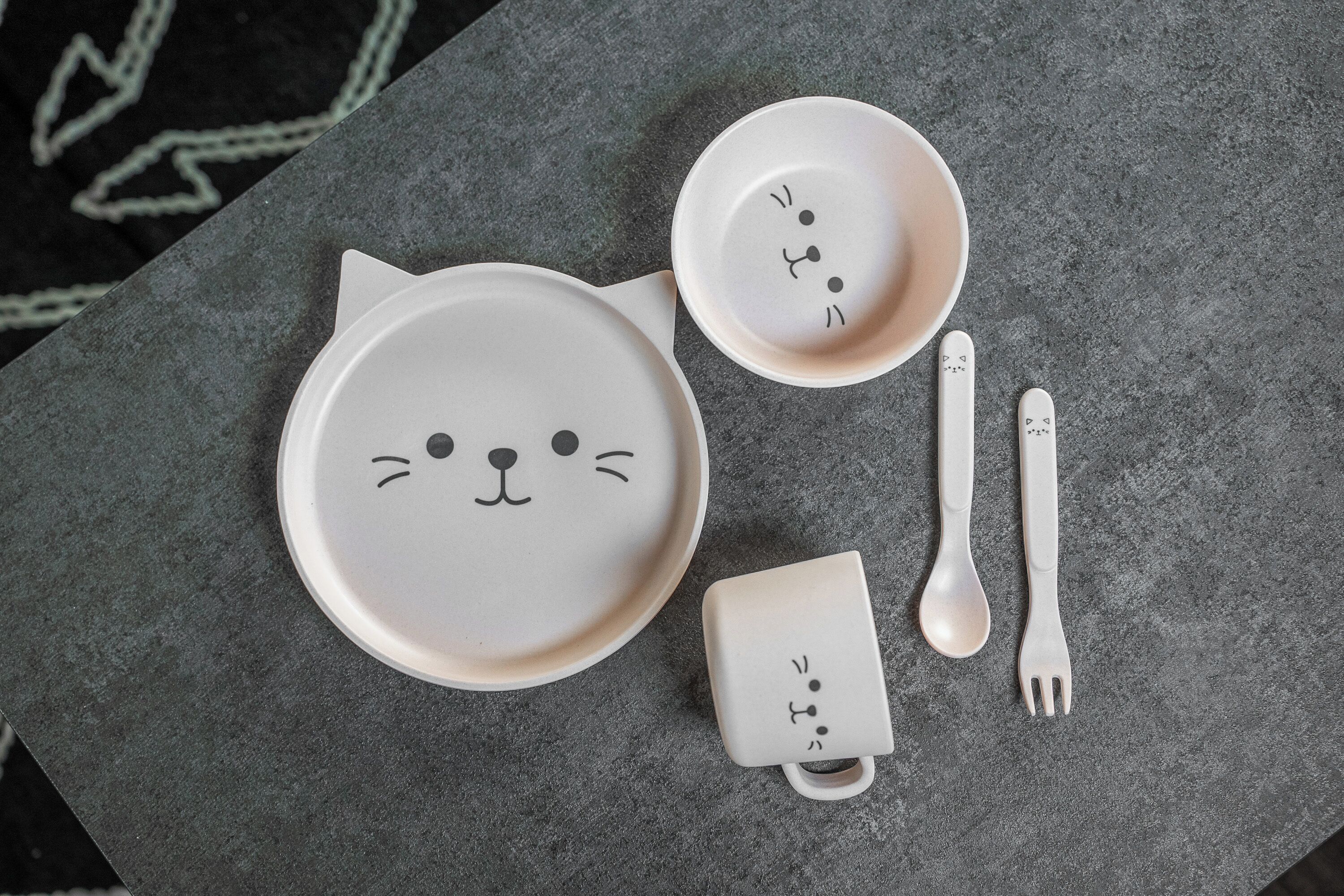 A set of cat-themed dinnerware on a gray surface.