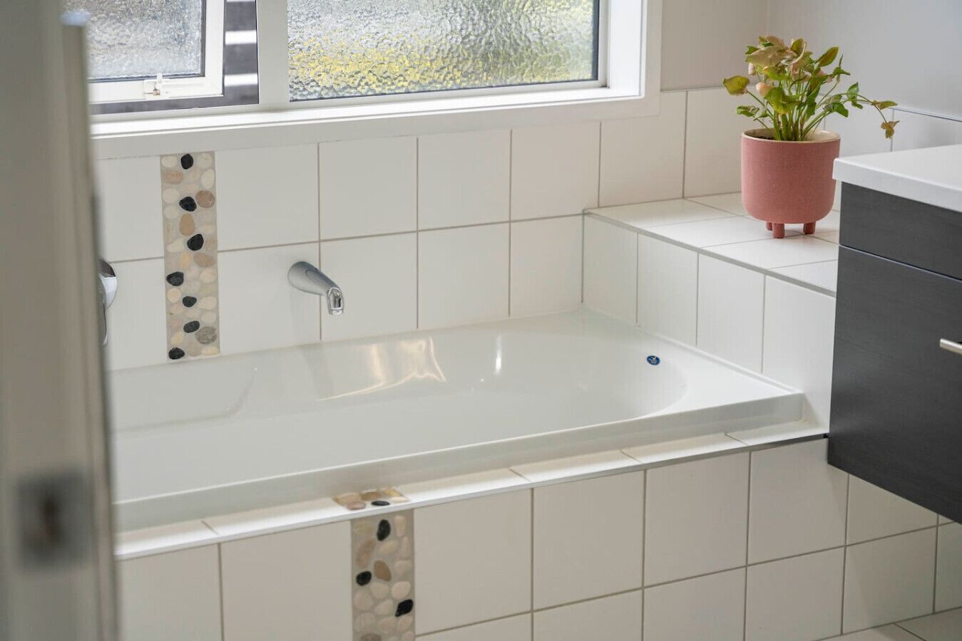Une salle de bain moderne avec une baignoire sur pieds, des carreaux blancs, une plante en pot et une fenêtre donnant sur un beau paysage.