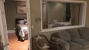 A bedroom with a bed, a wicker chair, and a grey sofa. - Creekside Chalet + Allstar Deluxe (Otego)