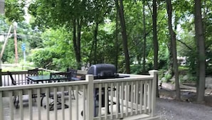 A deck with outdoor furniture and a grill, surrounded by trees. - Creekside Chalet + Allstar Deluxe (Otego)
