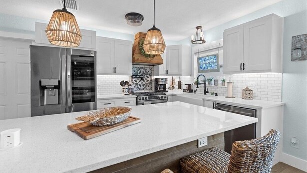 Een moderne keuken met witte kasten, een groot eiland en hanglampen.