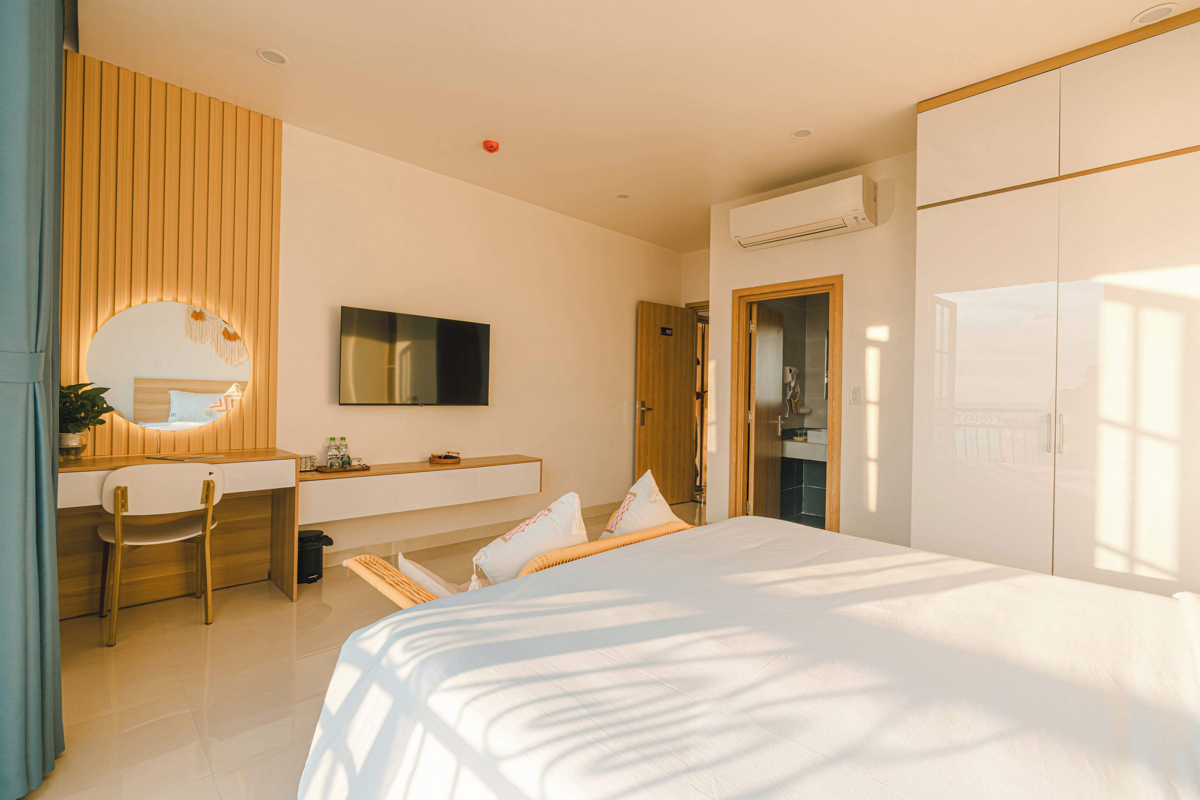 A modern hotel room with a bed, a desk, a chair, a mirror, and a wardrobe.