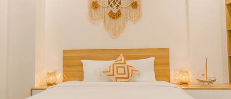 Una cama bien hecha con un cojín geométrico, un tapiz de macramé y dos lámparas de noche.