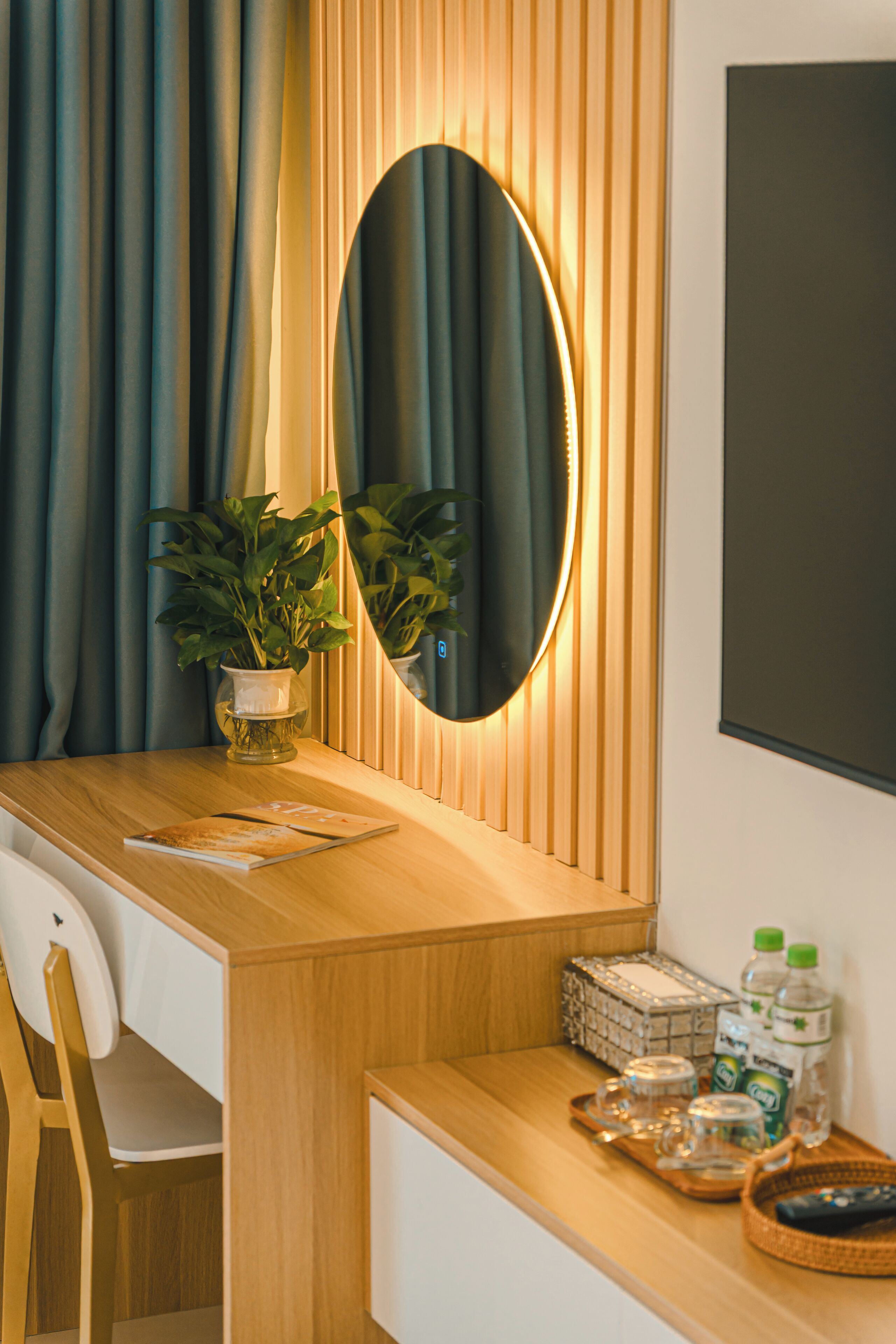 Een hotelkamer met een houten bureau, een potplant, een spiegel en een dienblad met flessen en glazen.