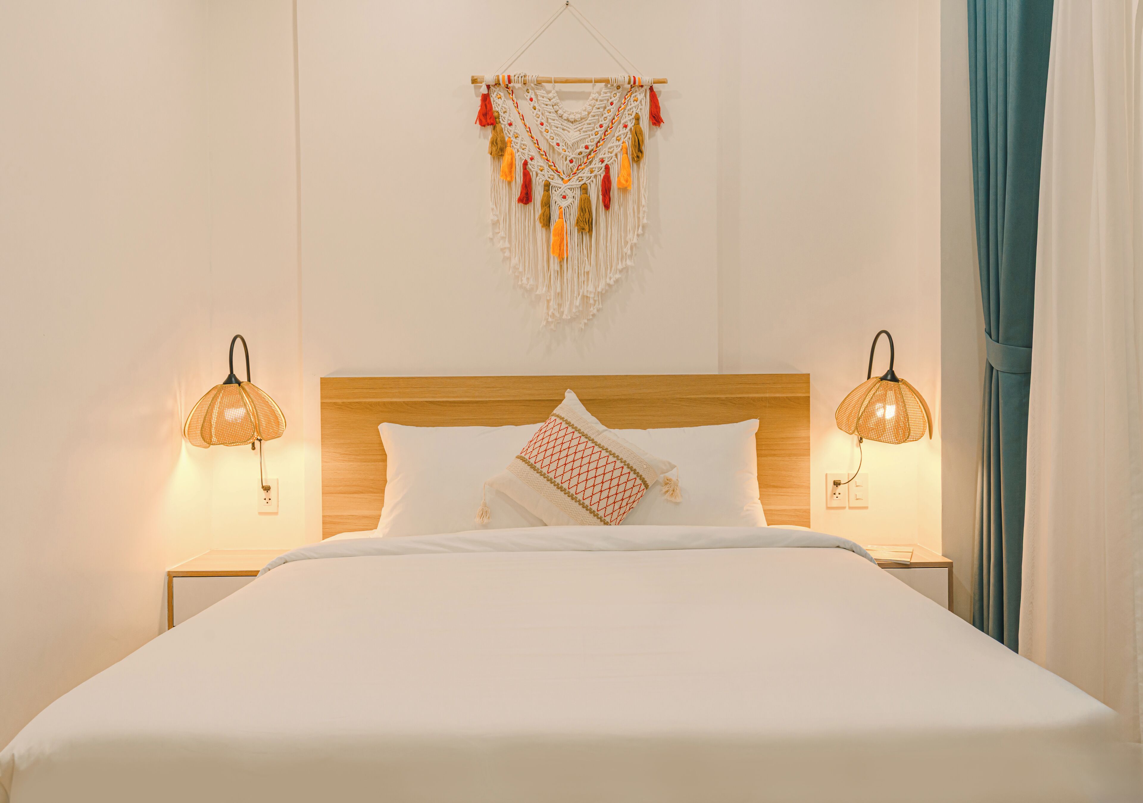 A neatly made bed with white linens, two bedside lamps, a wooden headboard, and a wall hanging above.