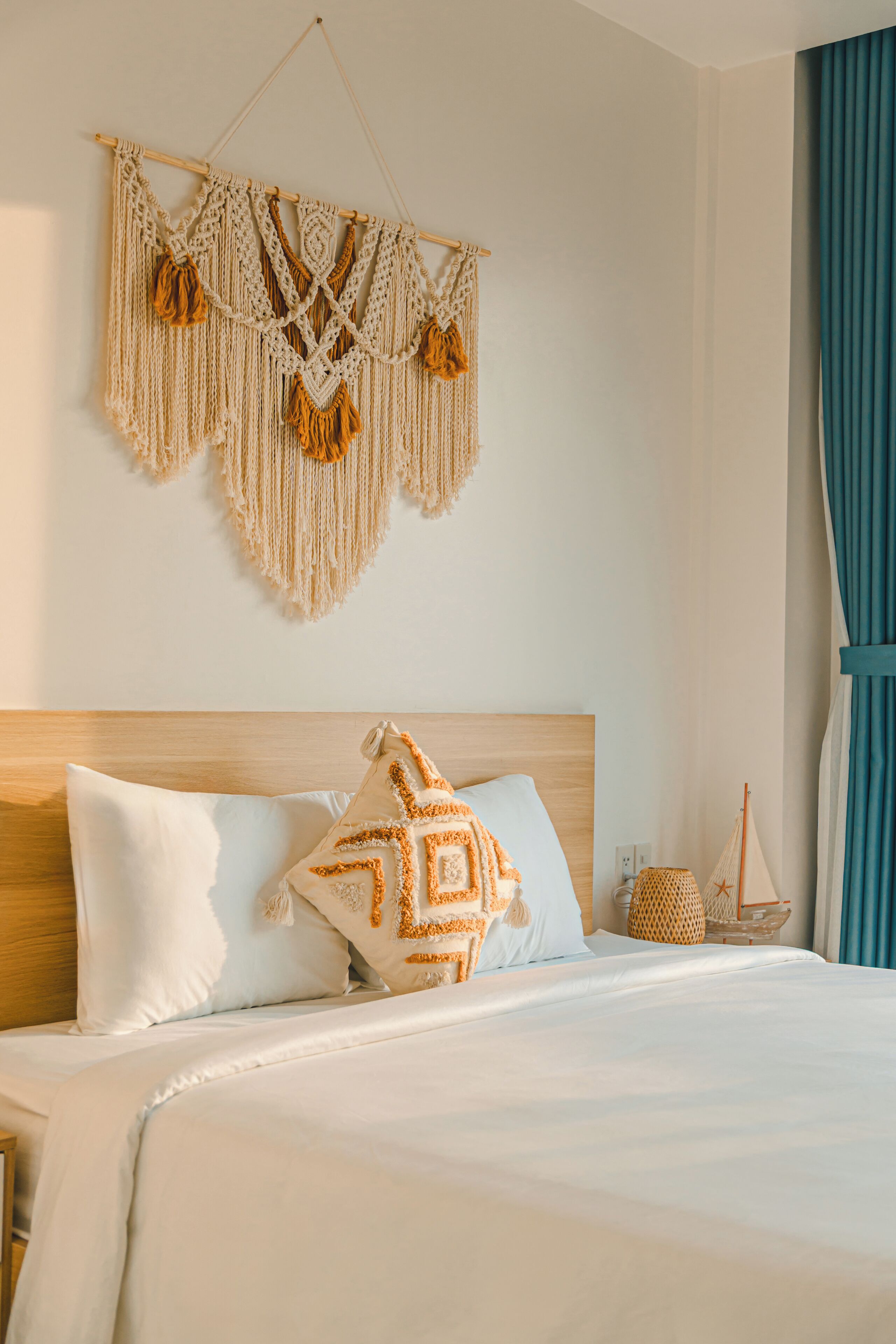 A neatly made bed with white bedding and a decorative macrame wall hanging above it.