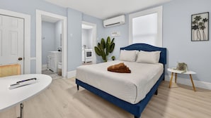 Ein Schlafzimmer mit einem Bett, einem weißen Schreibtisch, einem kleinen Tisch mit einer Pflanze und einem Topf mit einer Pflanze neben dem Bett.
