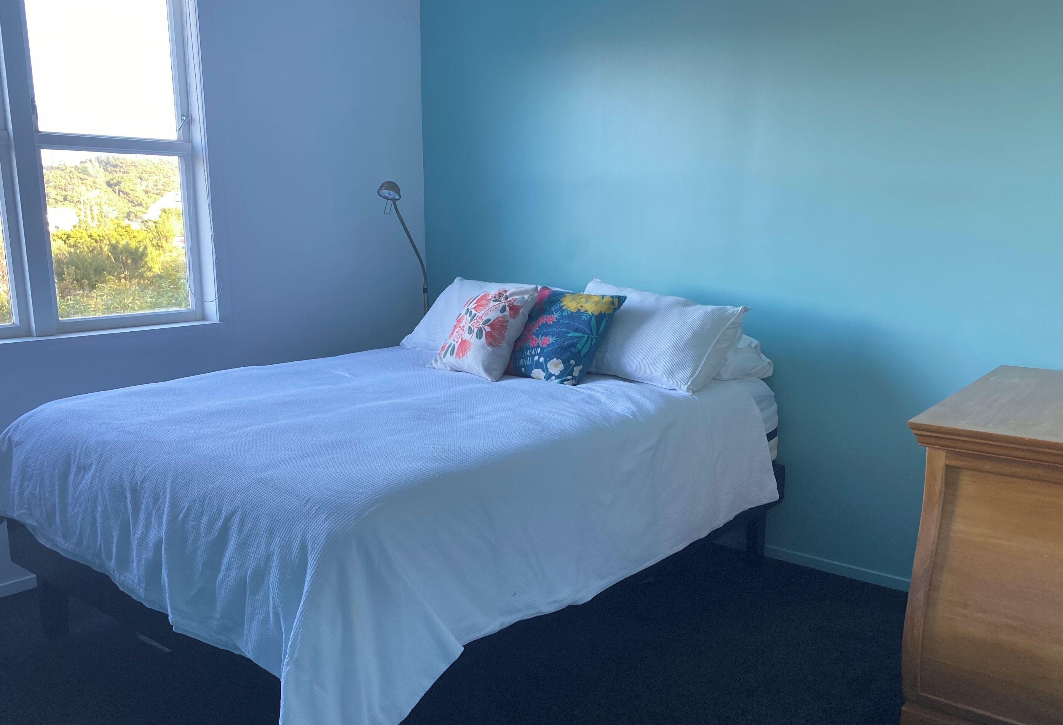 A bed with white bedding, a window with a view of greenery, and a blue wall.
