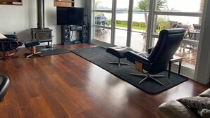 A living room with a large window, a fireplace, and a flat-screen TV. - Coastal cottage with serene views, near to all ammenities and beaches. (Paihia)