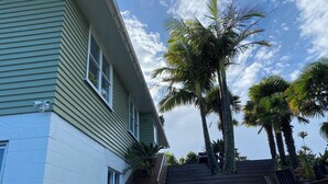 A two-story house with a green exterior and a wooden deck. - Coastal cottage with serene views, near to all ammenities and beaches. (Paihia)