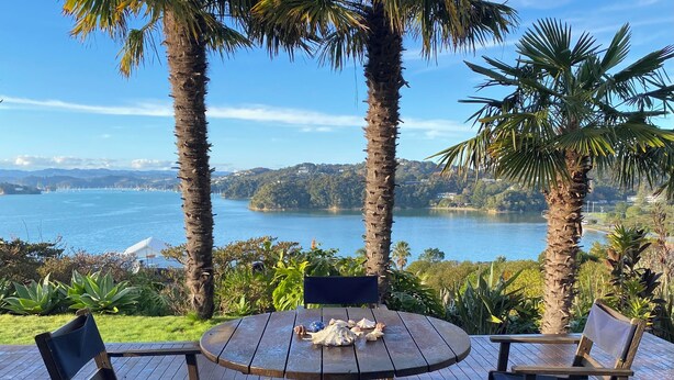 A wooden deck with a round table and four chairs, overlooking a lake with mountains in the distance. - Coastal cottage with serene views, near to all ammenities and beaches. (Paihia)