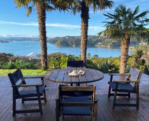 A wooden deck with a round table and four chairs, overlooking a lake with mountains in the distance. - Coastal cottage with serene views, near to all ammenities and beaches. (Paihia)
