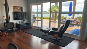A living room with a large window, a fireplace, and a view of the outdoors. - Coastal cottage with serene views, near to all ammenities and beaches. (Paihia)