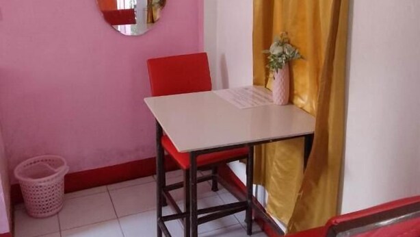 A small room with a table and two chairs, a mirror, a curtain, and a trash bin. - WJV INN CORDOVA 1 (Cordova)