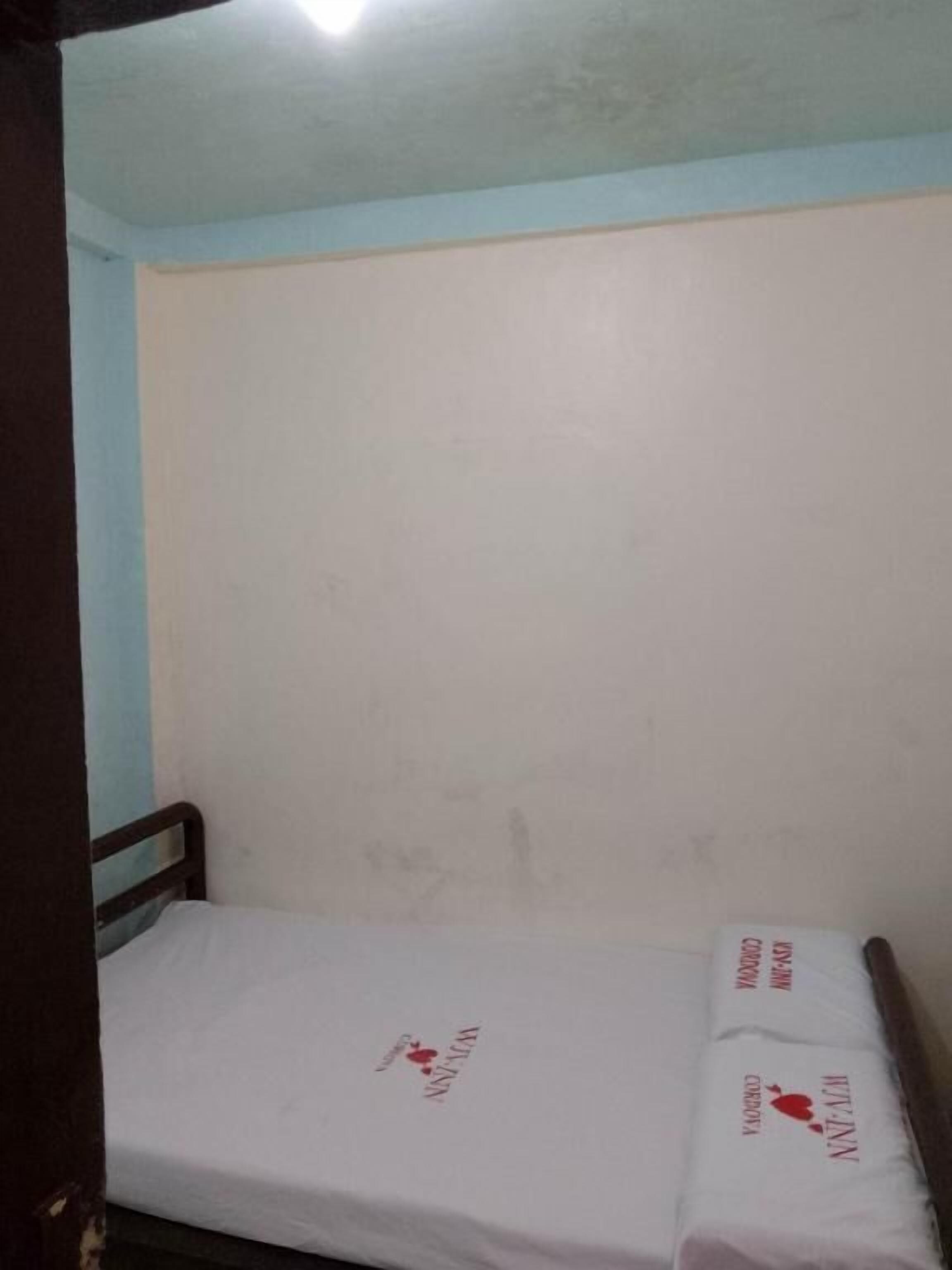 Habitació petita amb un llit individual, un matalàs blanc senzill i un capçal de llit de fusta.
