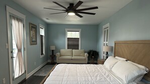 Une chambre à coucher avec un lit, un ventilateur de plafond, une fenêtre avec des stores, un canapé et une table de chevet.