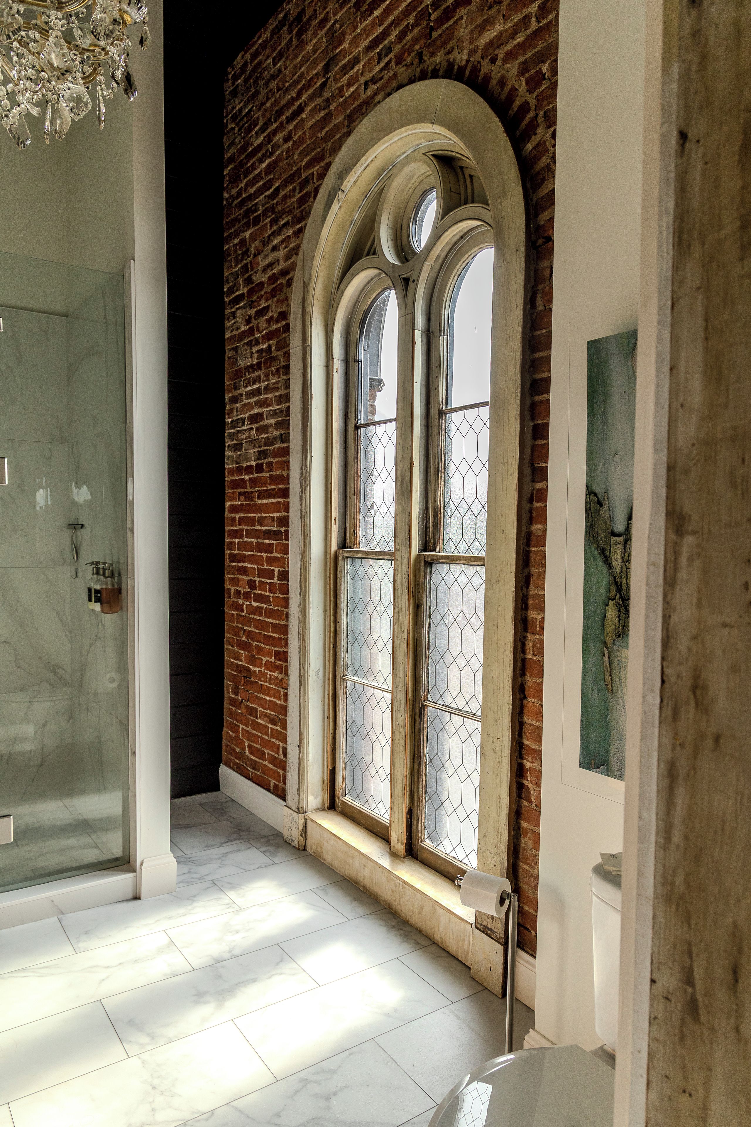 A room with a large arched window, a shower area, and a marble floor.