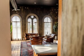 A room with a large table, leather sofas, and a patterned rug. There are three arched windows with curtains. - Light Filled Loft on Town Square. (Carlinville)