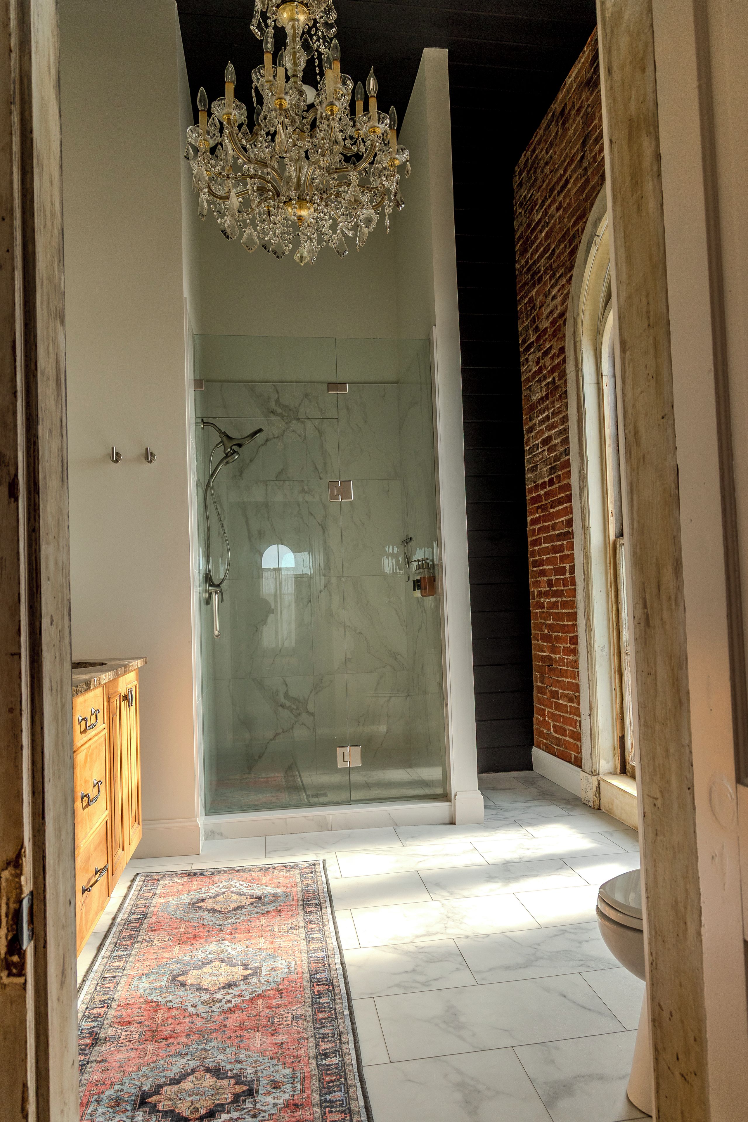 Een moderne badkamer met een glazen douche, een marmeren vloer en een kroonluchter.