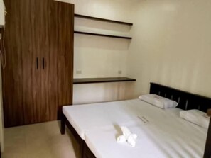 Une chambre avec une armoire en bois, un lit avec une literie blanche et une étagère au-dessus du lit.