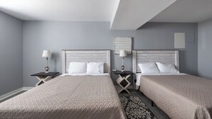 A hotel room with two beds, a nightstand with a lamp, a decorative wall piece, and a patterned rug.