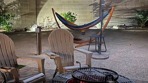 An outdoor patio with a fire pit, two Adirondack chairs, a hammock, and a patio umbrella. - CASA LINDA - quiet, peaceful 3 bedroom home in Mesa Del Sol. (Yuma)