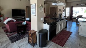 A spacious living area with a sofa, television, and a small wooden cabinet. A kitchen area with a sink and countertop is visible. - CASA LINDA - quiet, peaceful 3 bedroom home in Mesa Del Sol. (Yuma)