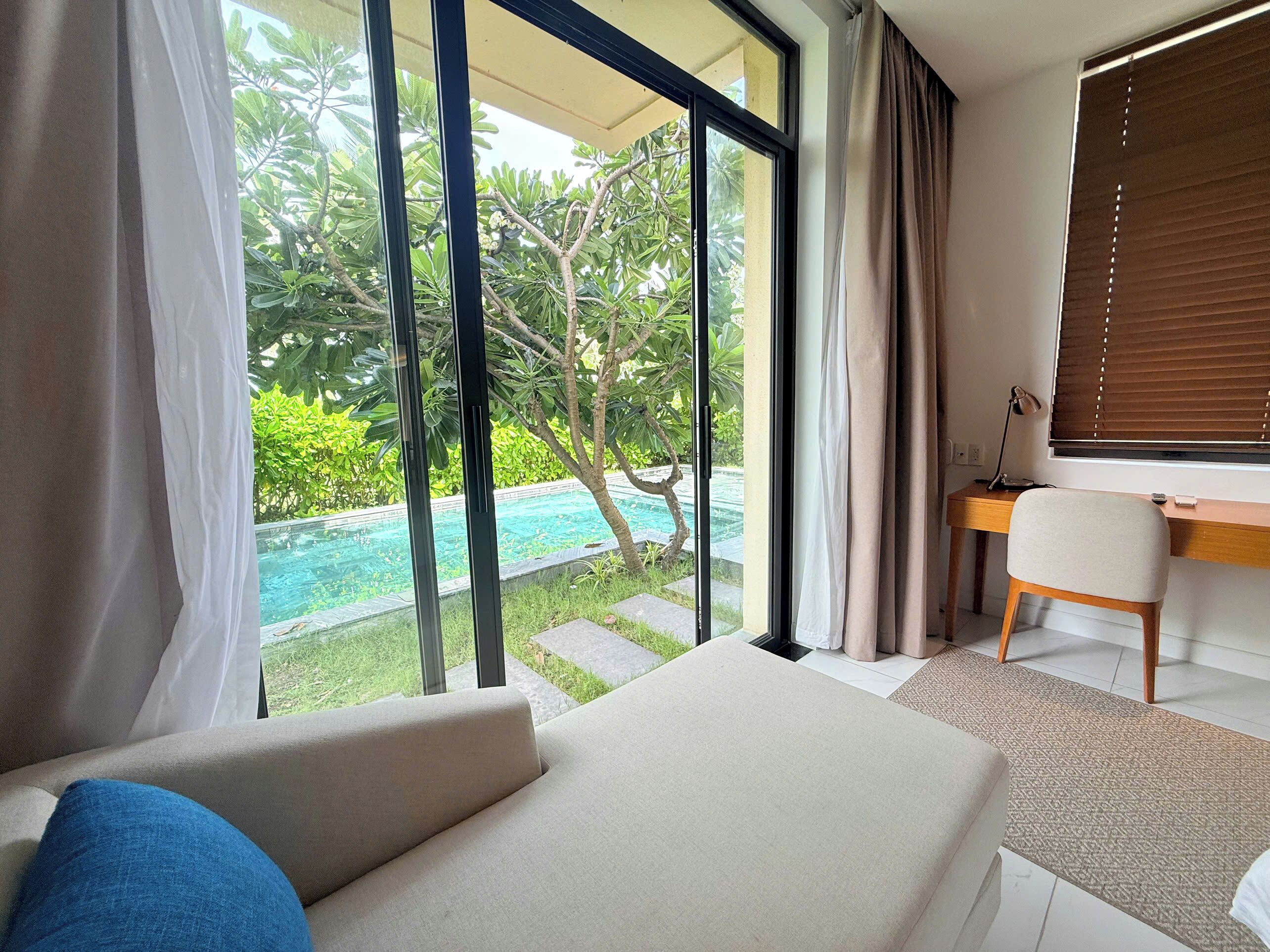 A modern bedroom with a large window, a bed, a desk, and a view of a swimming pool.