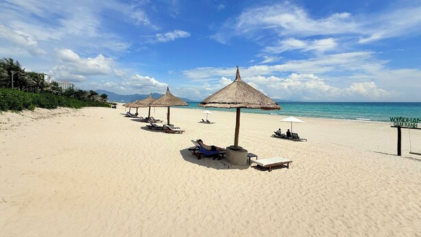 A beach with sun loungers and thatched umbrellas, a clear sky, and a sign indicating 'Wyldham (Tam Ranh)'. - Luxury Villa Beach Front (Cam Lam)