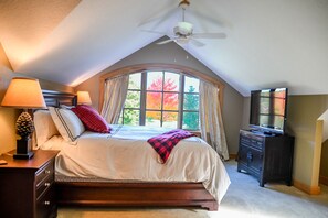 Ein Schlafzimmer mit einem großen Bett, einem Deckenventilator, einem Fernseher und einem Fenster mit Herbstlaub.