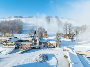 Ein verschneites Skigebiet mit einer Lodge, die einen markanten Glockenturm, Skipflanzen und eine verschneite Landschaft zeigt.