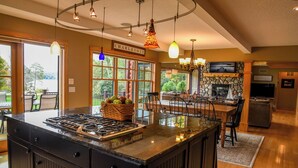 A kitchen with a large island, a stone fireplace, and a dining area with a view of the outdoors.