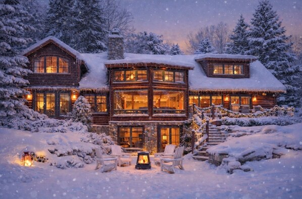 A log cabin with a stone chimney, multiple windows, and a snow-covered exterior.