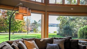 A modern living room with a sectional sofa, large windows, and a view of a lake and trees.
