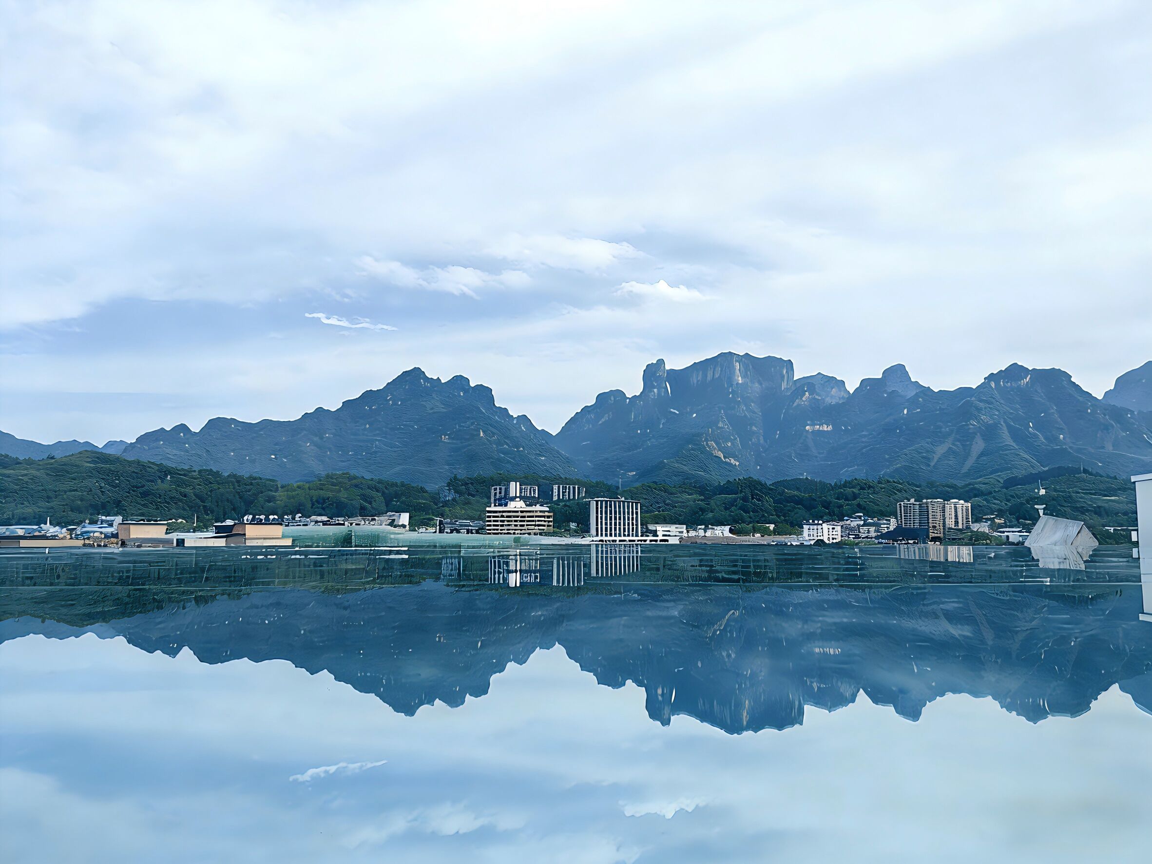 Um lago calmo refletindo montanhas e edifícios.