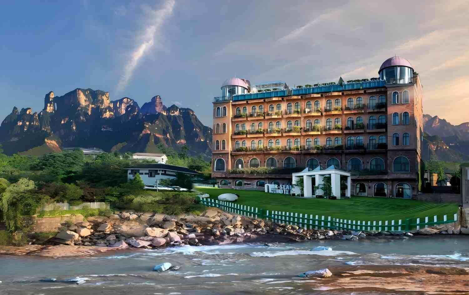 Un hotel con un edificio grande, un puente y montañas al fondo.