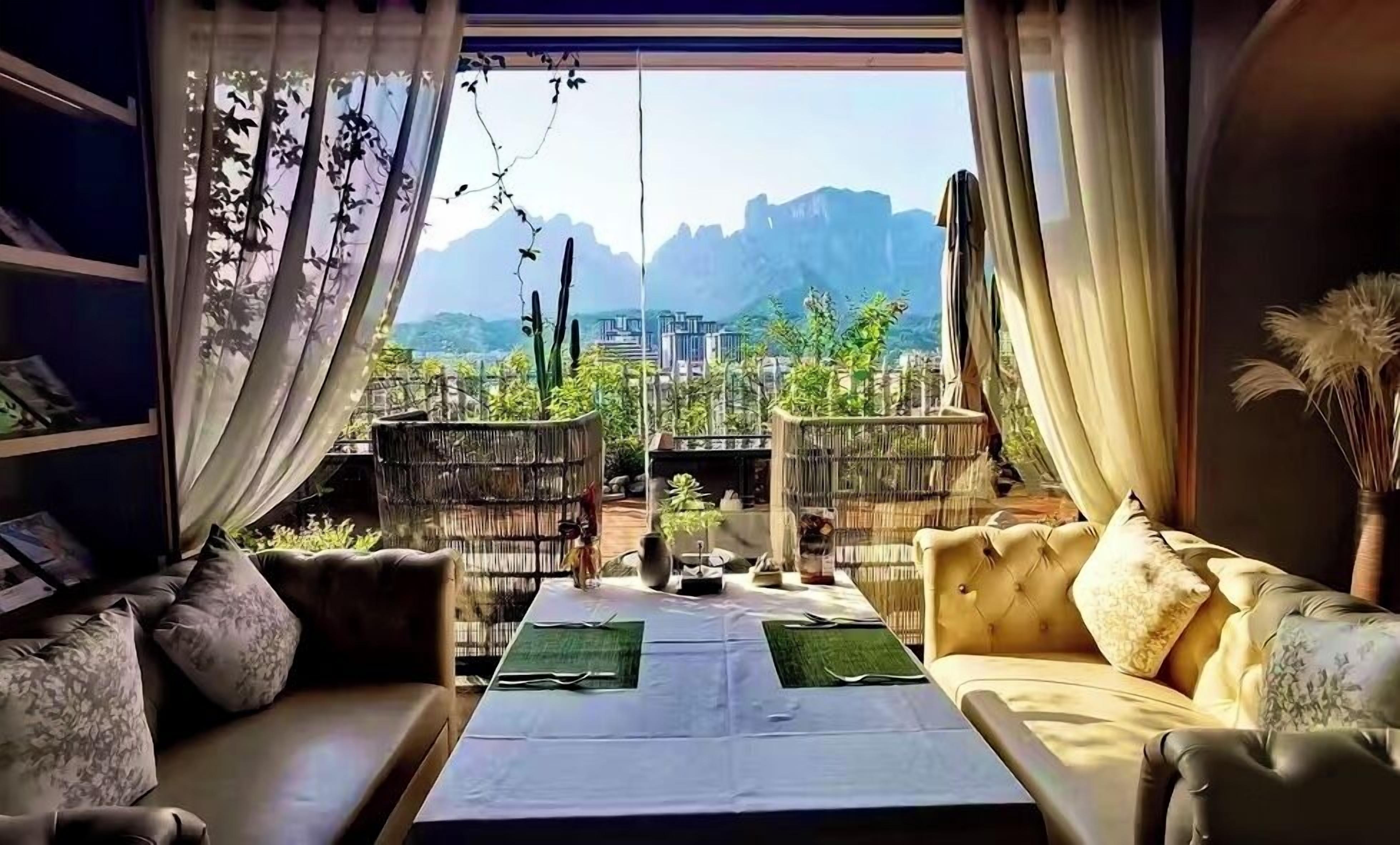 A room with a view of mountains, a sofa, a dining table, and a bookshelf.