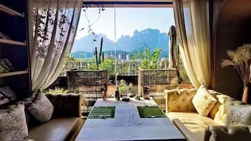 A room with a view of mountains, a sofa, a dining table, and a bookshelf.