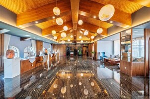 A spacious lobby with a polished marble floor, wooden ceiling beams, and modern pendant lighting.