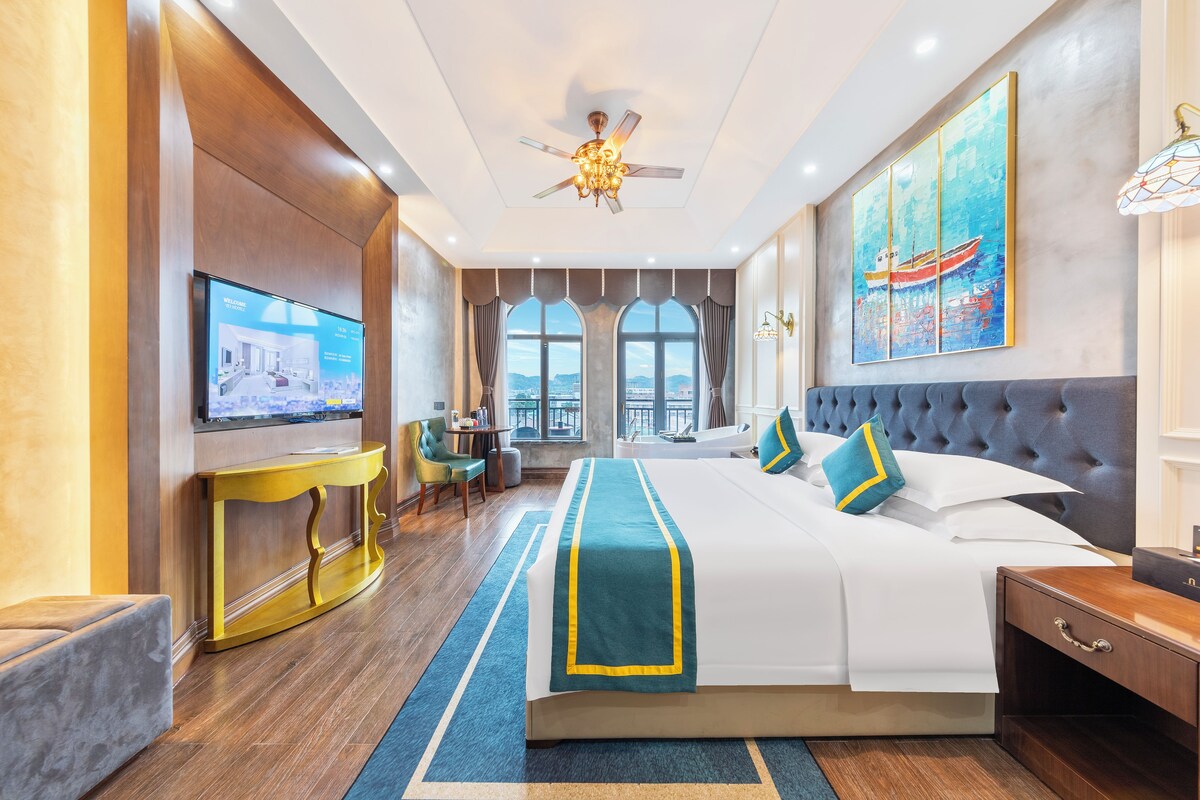 A hotel room with a large bed, a television, a desk, and a view of the city.