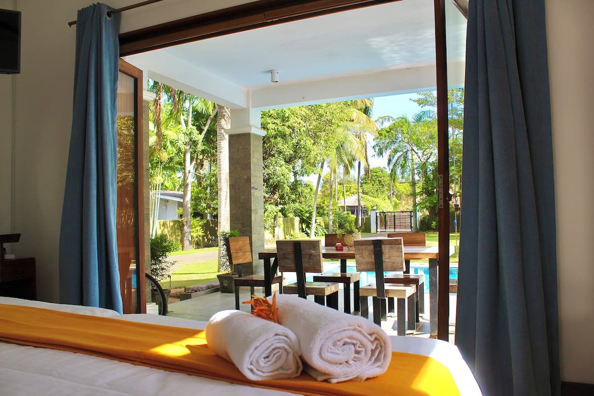 Habitación de hotel con cama, vista a una piscina y zona de estar al aire libre.
